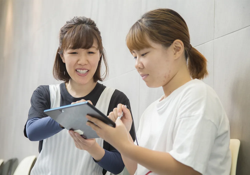 歯科医院のスタッフがタブレットの画面を見せながら患者に説明している様子